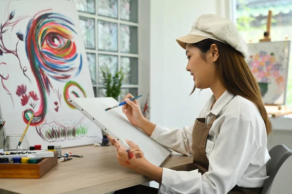 Young beautiful female artist painting on blank canvas. Hobby, art and people concept.