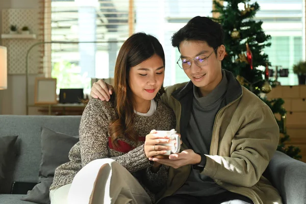 ロマンチックなアジアのカップルは 快適なソファでリラックスし ホットチョコレートを飲み 自宅でクリスマスの朝を楽しむ — ストック写真