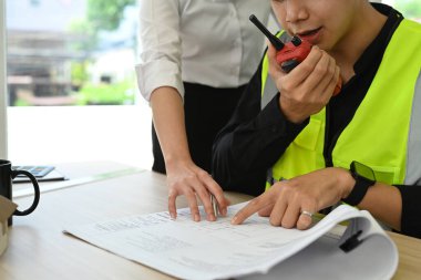 İnşaat planları üzerinde çalışan mühendis telsizle iletişim kuruyor..