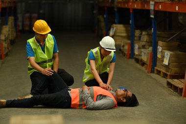 Erkek yönetici beton zeminde baygın yatıyor ve iş arkadaşları yaralılara yardım ediyor ve onlara ilk yardımı yapıyor..