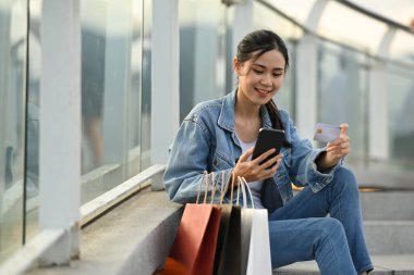 Çatıdaki merdivenlerde çantalarla oturan güzel bir kadın ve faturayı internet üzerinden akıllı telefondan ödeyen güzel bir kadın..