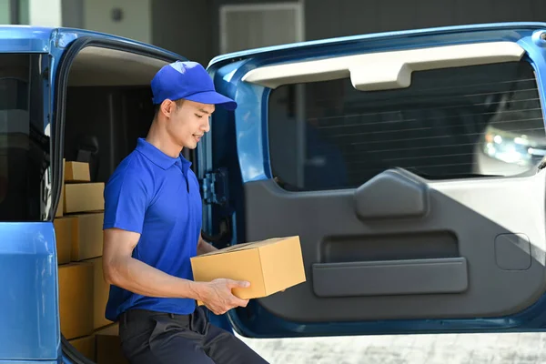 Asian man courier checking information on cardboard box while sitting open delivery van. Shipping and delivery service concept.
