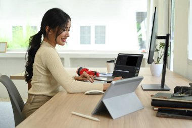 Modern ofisteki bilgisayar yazılımıyla video ve ses görüntülerini düzenleyen kadın serbest yazar yan görüntüsü.