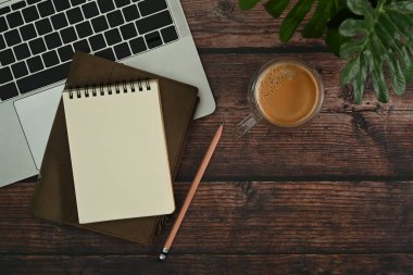 Düz yatış, boş not defteri, dizüstü bilgisayar kahve fincanı ve ahşap masadaki ev bitkisi..