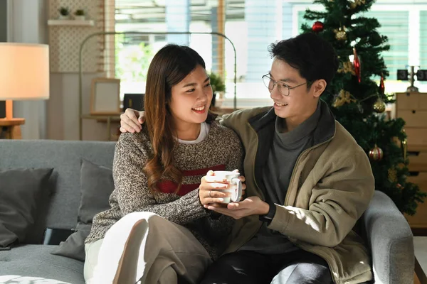 Romantic couple relaxing on comfortable couch, drinking hot chocolate and enjoying winter morning at home.