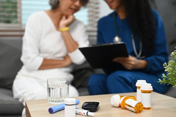 Pill bottles on table with healthcare worker and senior woman sitting on background. Elderly healthcare, pharmaceutical concept.