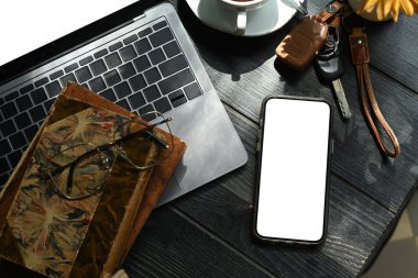 Akıllı telefon, dizüstü bilgisayar, kitap ve kahve fincanının kırsal ahşap masa üzerindeki üst görüntüsü.