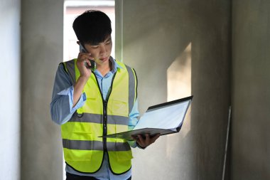 İnşaat alanında dikilip cep telefonuyla konuşan yansıtıcı ceketler giyen mühendis..