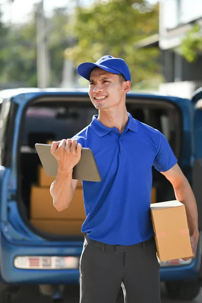 Portrait of delivery man carrying cardboard parcel and using digital tablet. Delivery service, post and shipping concept.