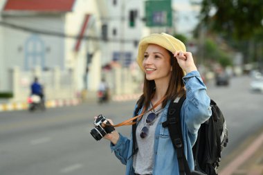 Sırt çantalı ve dijital kameralı genç bayan turist şehir caddesinde duruyor. Blogcu, tatil ve seyahat kavramı.