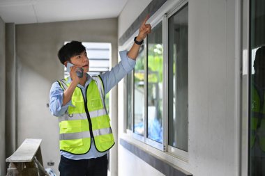 İnşaat alanında otururken cep telefonuyla konuşan sarı yelekli bir mimar resmi.