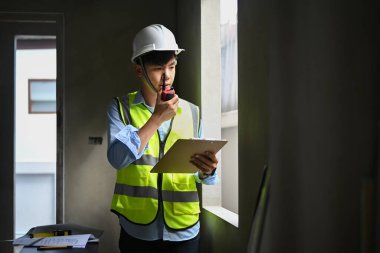 Asyalı adam site yöneticisi iş arkadaşıyla telsizle konuşuyor ve inşaat alanında duruyor..