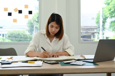 Architect woman working on design of a construction plan and examining construction plans at office.