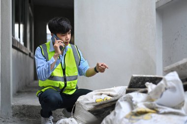Young asian man inspectors talking on mobile phone and checking building material at construction site.