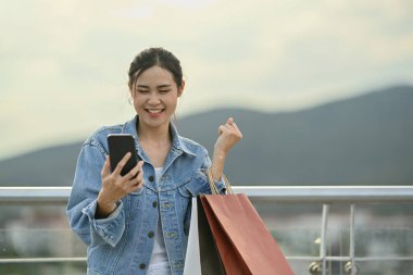 Surprised asian woman looking on mobile phone and feeling excited, screaming with joy celebrate victory success.