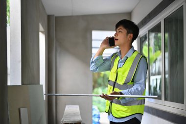 Image of engineer man talking on mobile phone with colleague while standing at construction site.