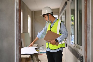Asian engineer man planning development details, examining plans at construction site. Engineer, construction concept.