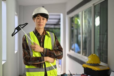 Portrait of asian man worker in safety helmet and reflective vest standing in construction site and looking at camera.