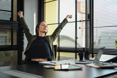 Happy caucasian female worker stretching arms, relaxing on comfortable office chair in modern office workplace.
