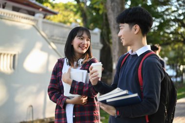 Two smiling college student walking after to college building and discussing the project or sharing the ideas.