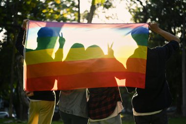Group of young activist with pride rainbow flag on foreground, supporting LGBTQ pride. LGBT community concept.