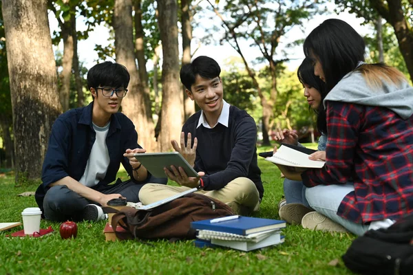Group of university students learning together while sitting under the tree. Relationship, youth and community concept.