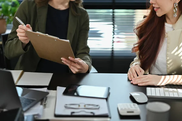 Cropped shot of two female marketing or sales executives discussing project results and planning work at office.