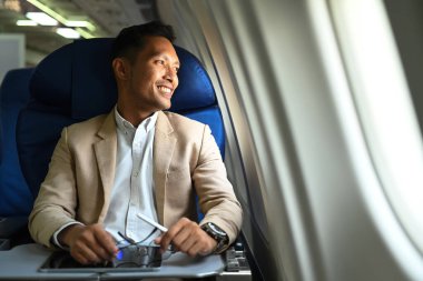 Satisfied businessman passenger sitting comfortable seat and looking out through window of the airplane.