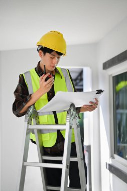 Engineer man in safety helmet yellow vests holding blueprints and walkie talkie standing in construction site.