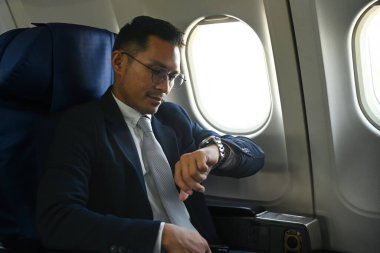 Successful businessman in elegant suit checking arrival time on his watch during business travel flight.