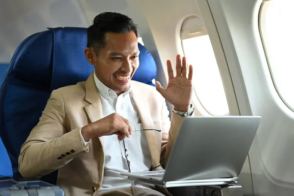 Image of millennial businessman having video call on laptop, using wireless connection on board in an airplane.