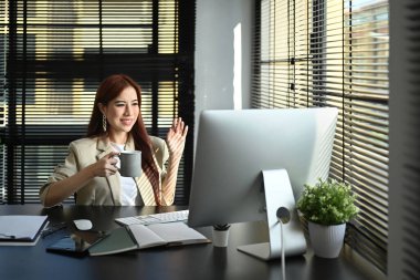 Attractive asian female entrepreneur waving hand, talking on video call on computer.