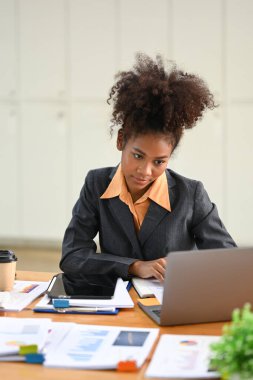Smiling African female manager using laptop and working with financial docent in her personal office.