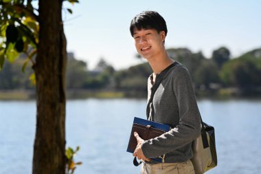 Portrait of man student man standing with lake with mountains sunny landscape on background. People and recreation in nature. 