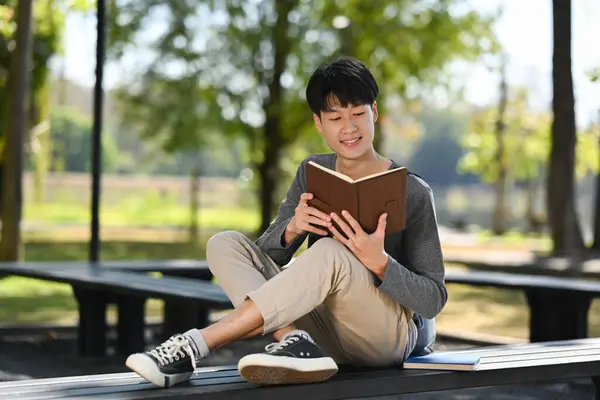 Young Asian Man Student Reading Interesting Book While Sitting Bench — Zdjęcie stockowe