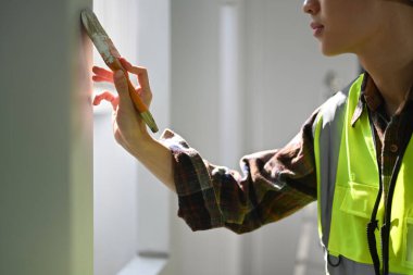 Cropped image of male painter in yellow vest holding painting brush painting a white wall. Home renovation concept.