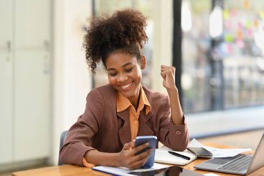 Satisfied African American reading good news in email or social network message on her mobile phone.