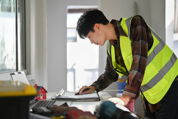 Engineer or building inspector in yellow vest checking and inspecting progressing work in construction site.