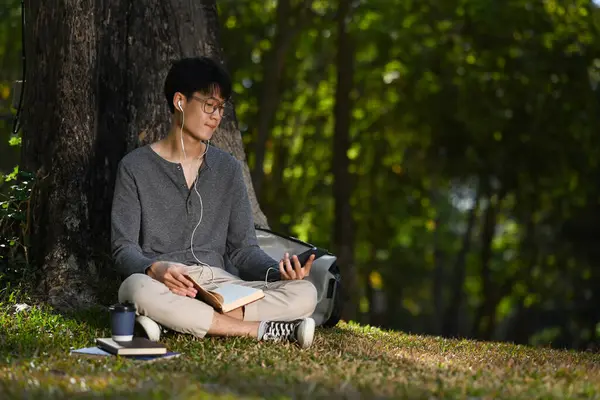 Teenage Asian Man Listening Music Earphone Using Mobile Phone Tree — Zdjęcie stockowe
