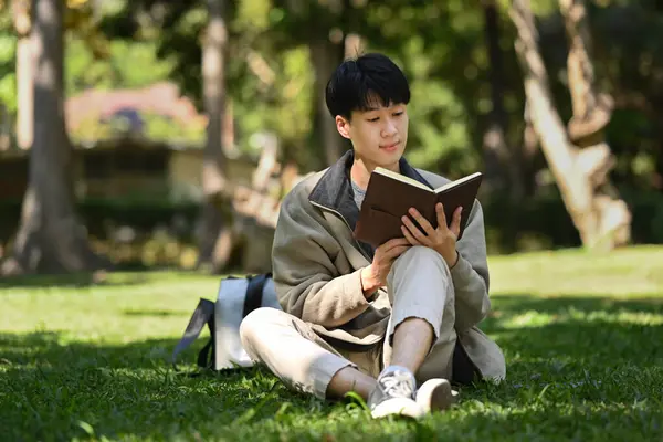 Happ Young Asian Man Reading Interesting Book While While Sitting — Zdjęcie stockowe