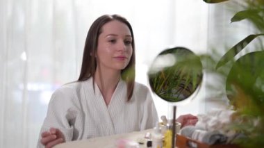 Caucasian woman taking off paper sheet mask from her face and touching it gently, satisfied with results.