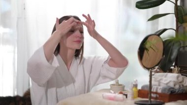 Caucasian woman applying sheet mask and rubbing her face with her fingers. Beauty and self care concept.