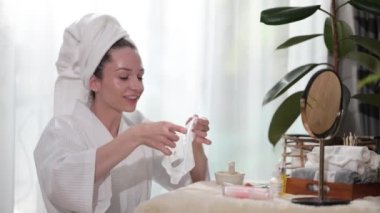 Beautiful caucasian woman wearing bath towel on head applying in sheet face mask. Beauty treatment concept.