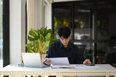 Professional businessman using laptop and comparing corporate income for previous year with current one at office desk.