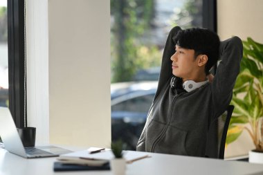 Satisfied man freelancer holding hands behind head and looking through window, enjoy resting at workplace.