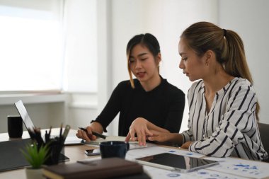 Two creative entrepreneurs discussing business strategy and using laptop computer at office desk.