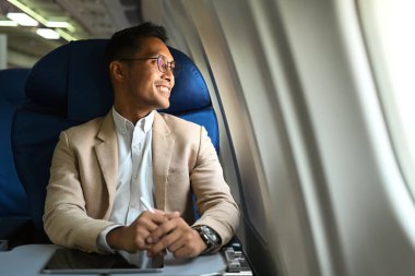Satisfied businessman in elegant luxury suit looking through window of the airplane during business travel. 