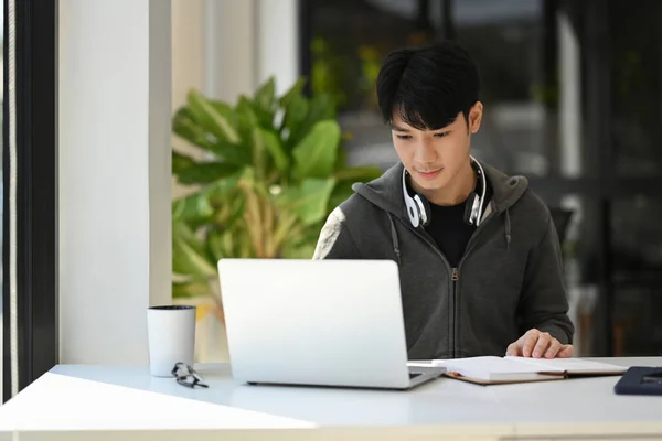 Young man freelancer in casual wear using laptop, working remotely from home.