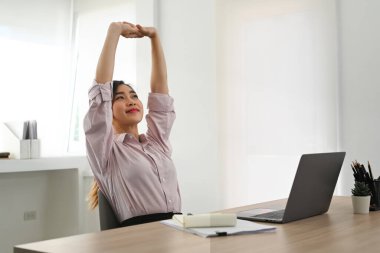 Relaxed asian woman office worker stretching her arms above her head at comfortable office chair.
