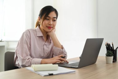 Pretty asian female executive manager typing on laptop computer, working in contemporary corporation office.